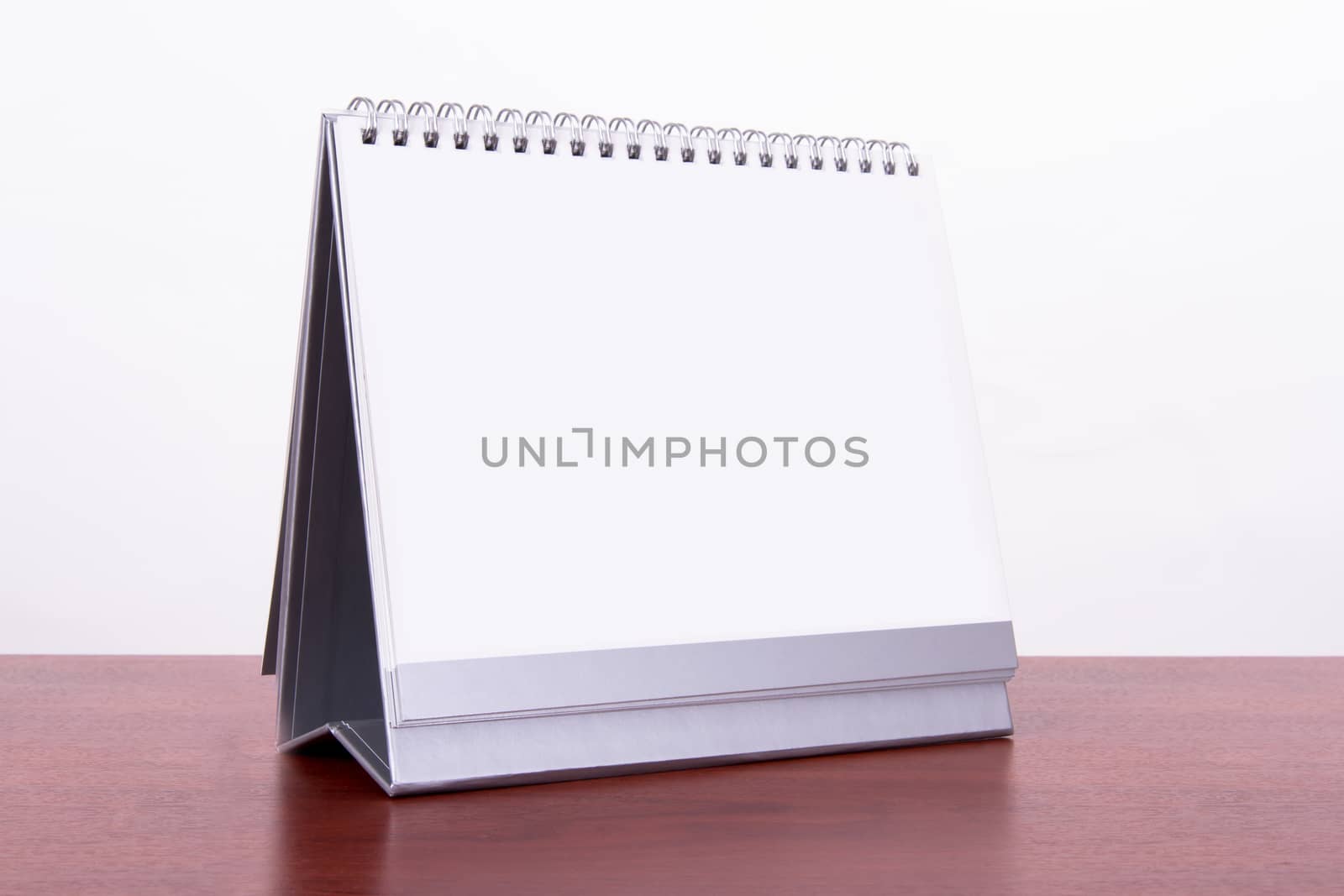 Single blank desk calendar on wooden table, isolated on white background.
