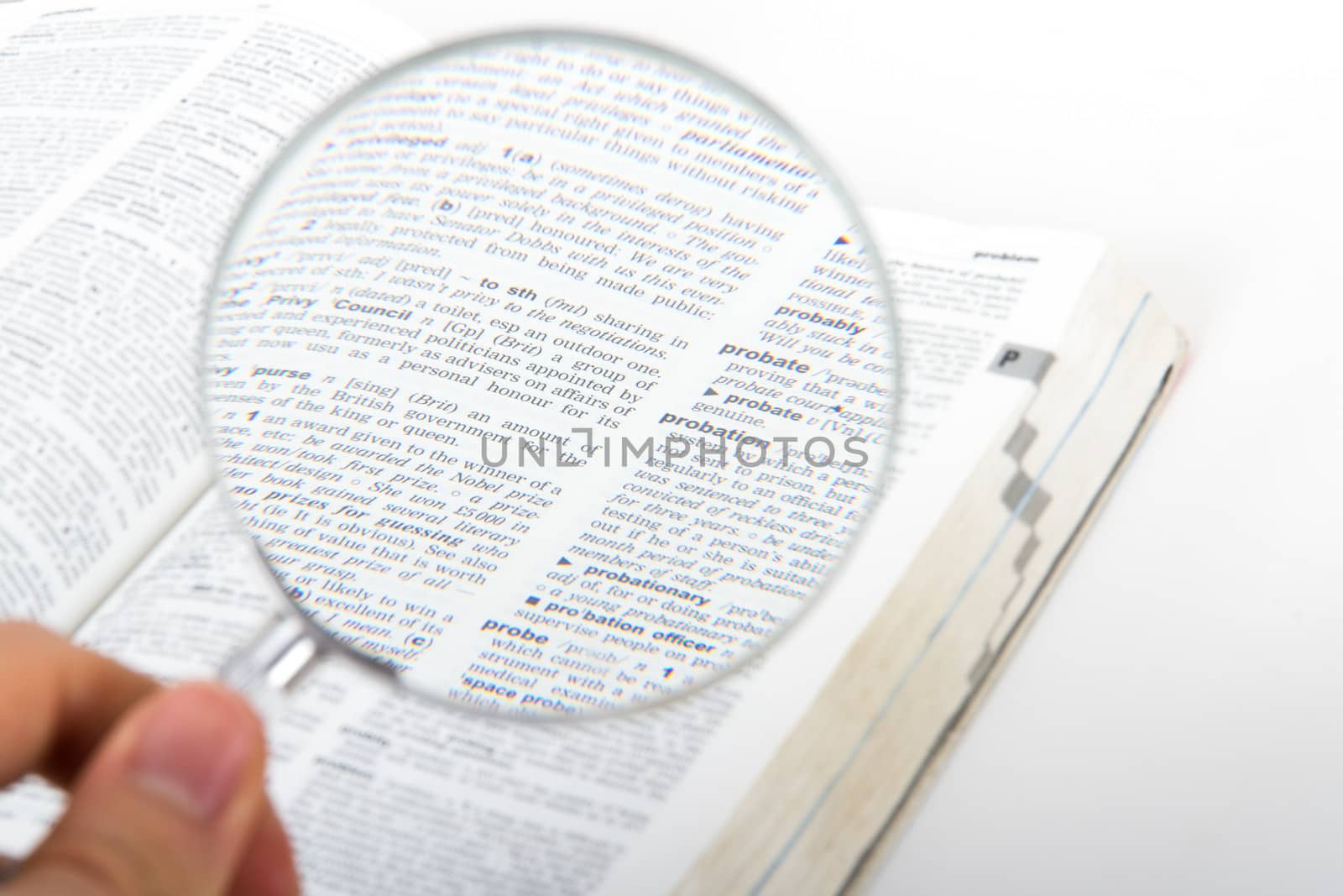 Hand holding magnifying glass, examining dictionary page, isolated on white background.