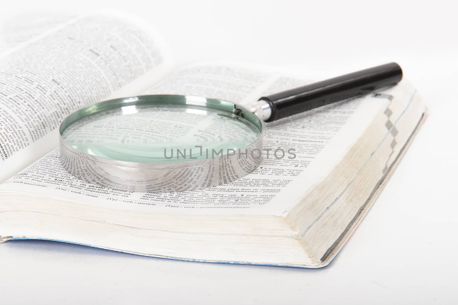 Classic style magnifying glass on open dictionary book, isolated on white background.
