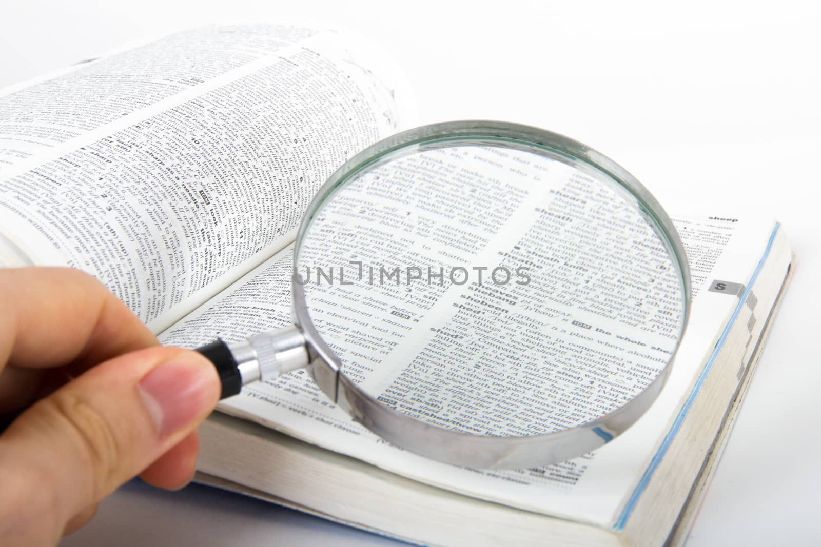 Hand holding classic style magnifying glass, searching for a word on open dictionary book, isolated on white background.