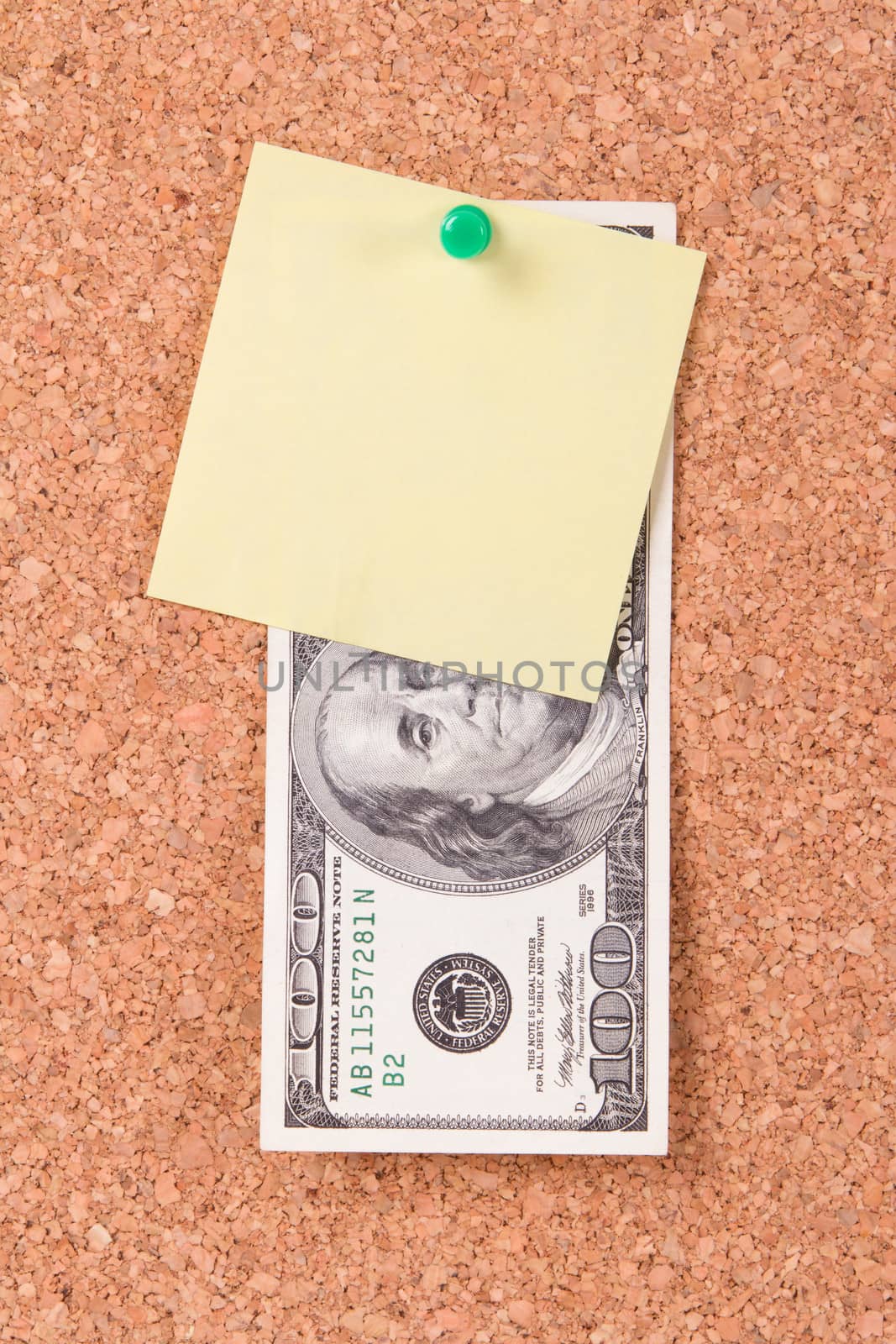 One hundred dollar bill and blank, empty yellow sticky post affixed to cork board with green pin.