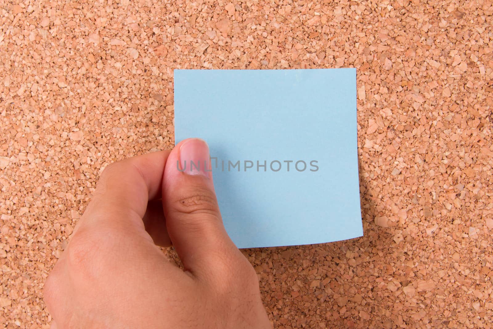 Hand and blank, blue sticky post it note for your message on cork bulletin board.