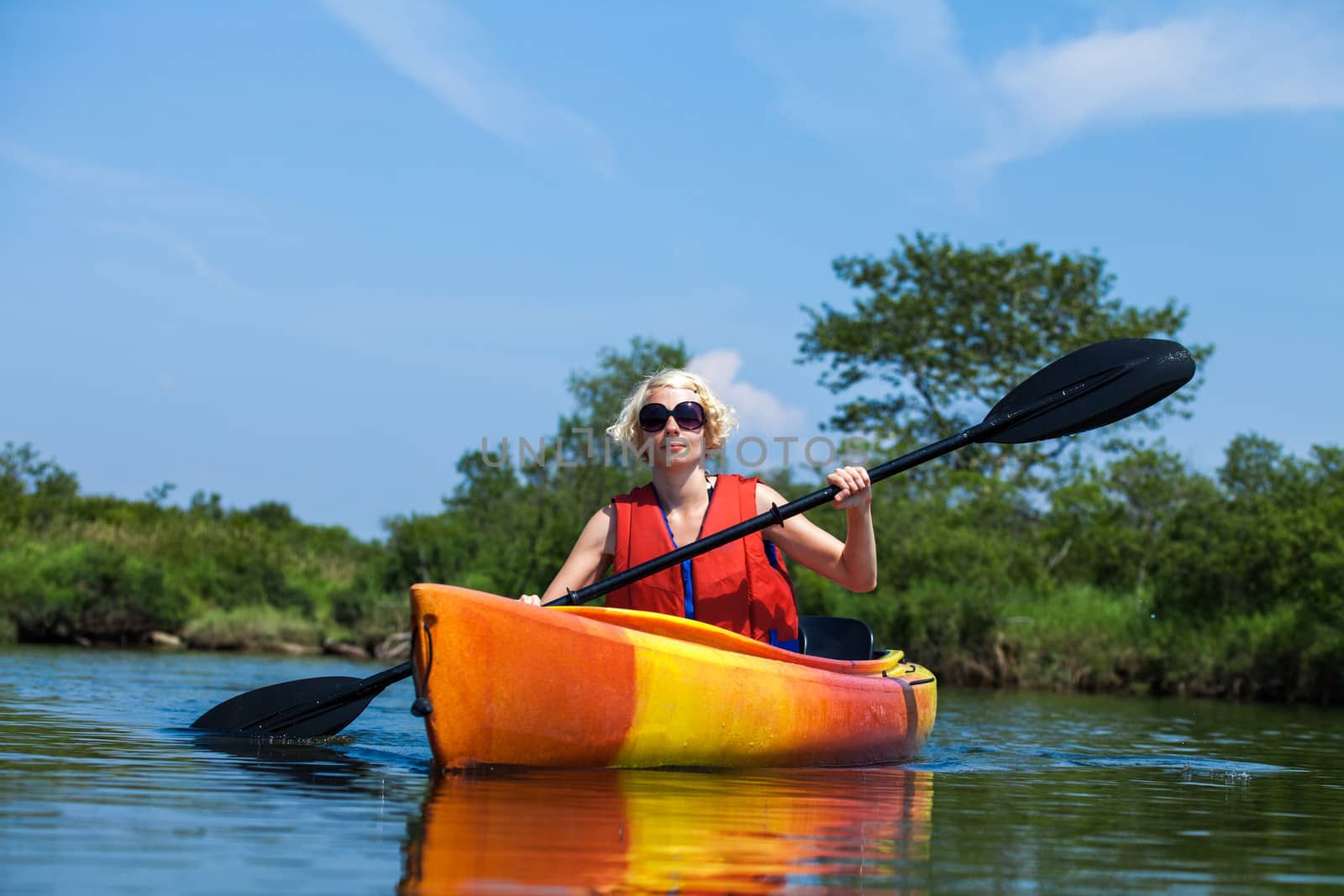 Woman With Safety Vest Kayaking Alone on a Calm River by aetb