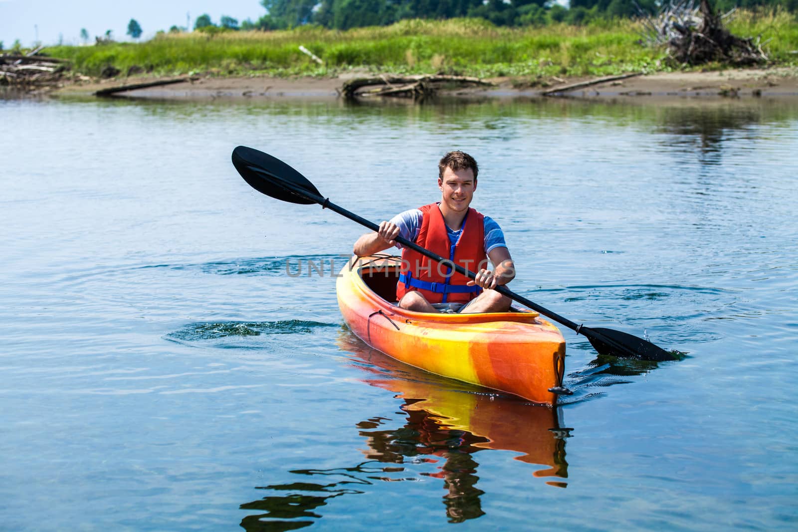 Young Man Kayaking Alone on a Calm River and Wearing a Safety Vest