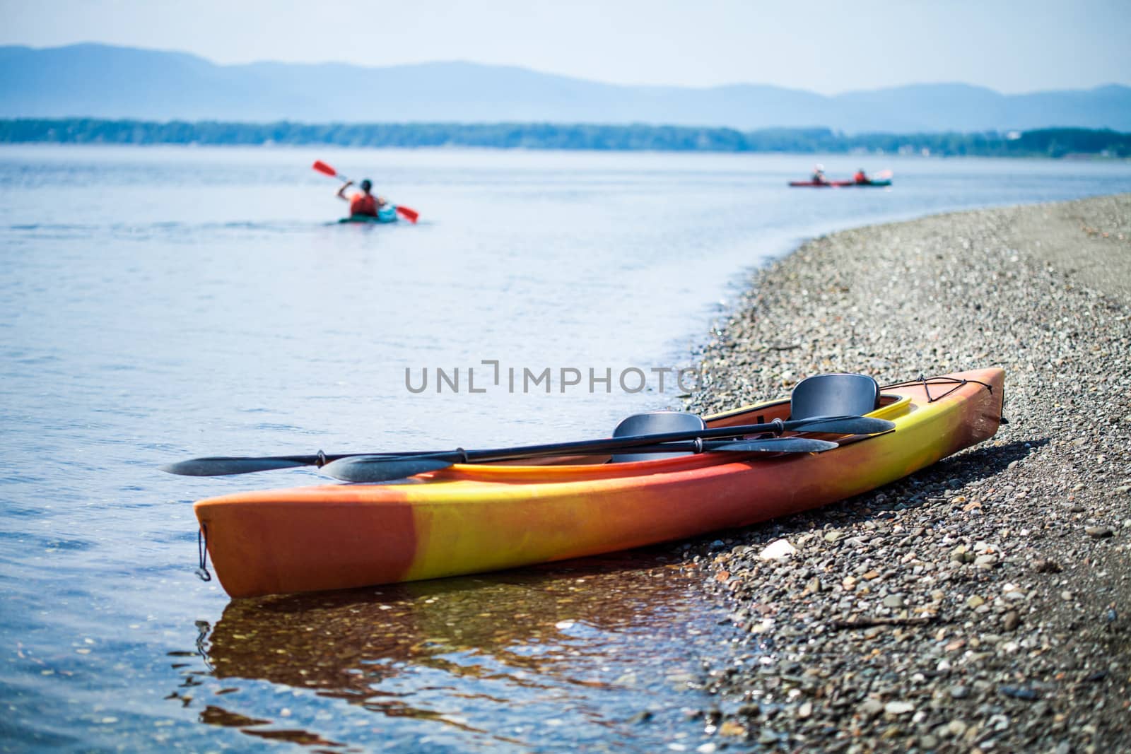 Orange and Yellow Kayak on the Sea Shore During a beautiful Day of Summer with Unrecognizable People Kayaking in the Background