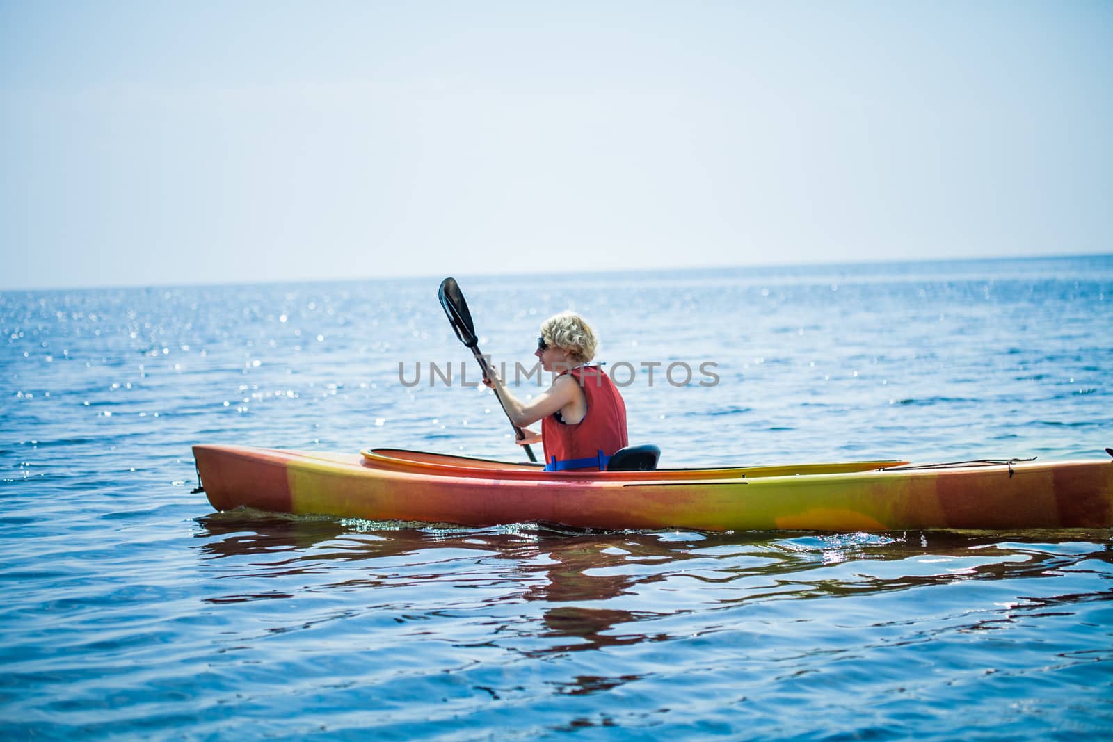 Woman With Safety Vest Kayaking Alone on a Calm Sea by aetb