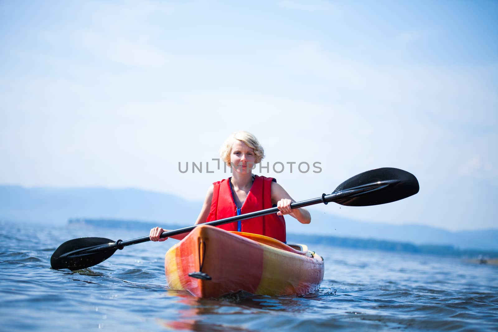 Young Woman Kayaking Alone on a Calm Sea and Wearing a Safety Vest