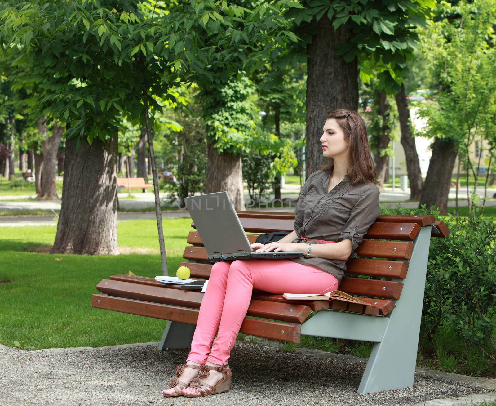Young woman sitting on a bench in a park and working on a laptop.