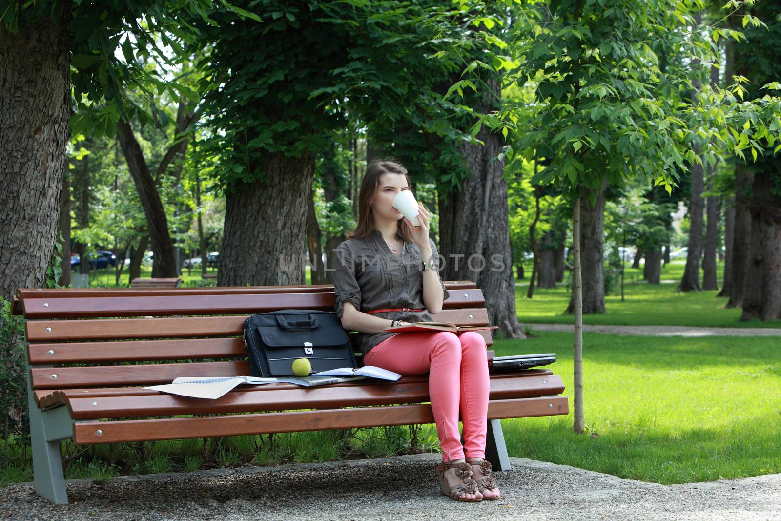 Young student woman drinking coffee while studying outdoor in a park.