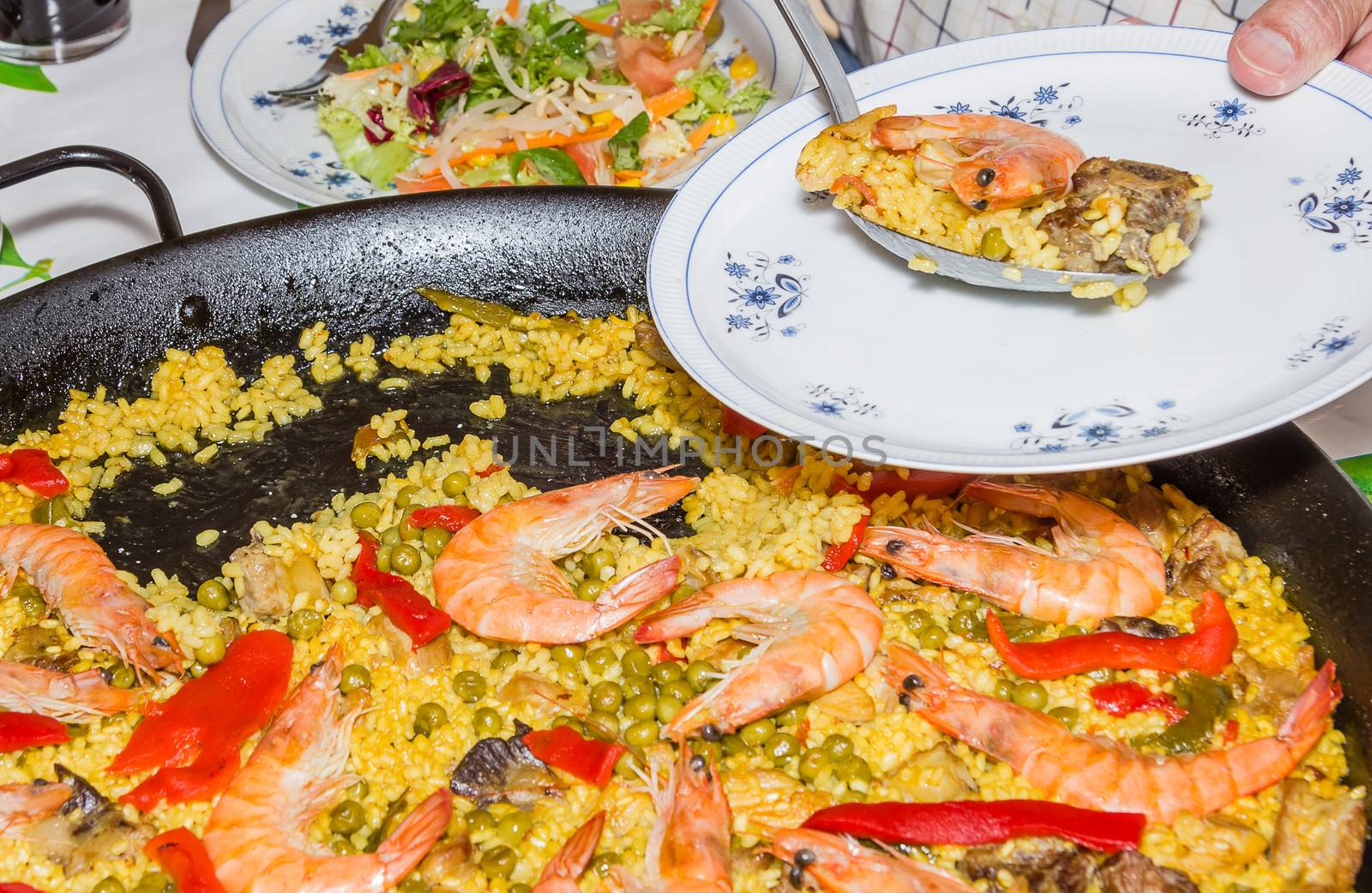 Serving traditional spanish paella cooked in a pan, with yellow rice and seafood