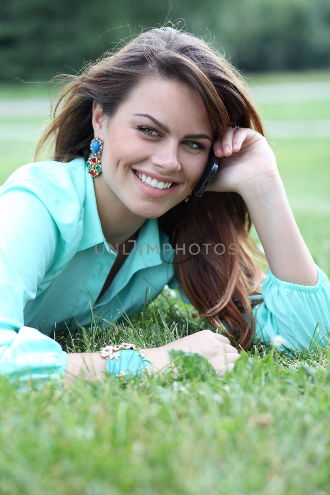 Young woman lying on the grass with phone in hand by andersonrise