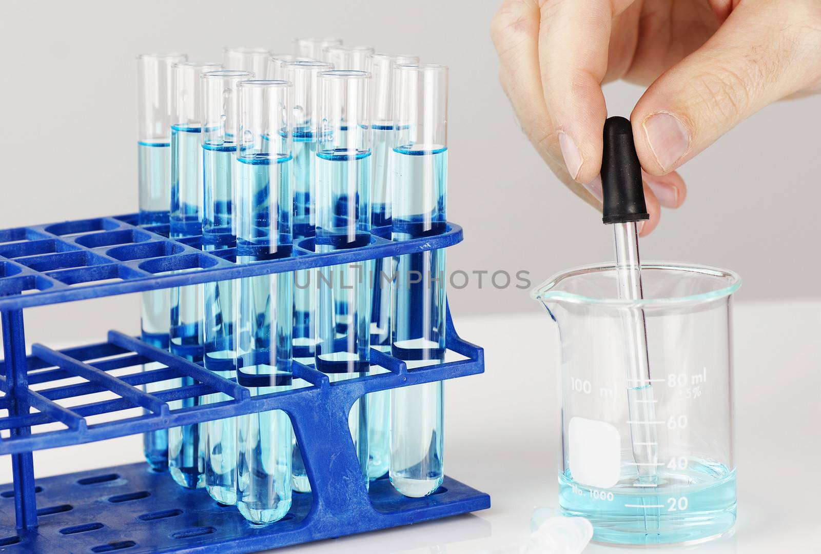 Test tubes with blue liquid, man hand with dropper: chemistry, biology or other science concept