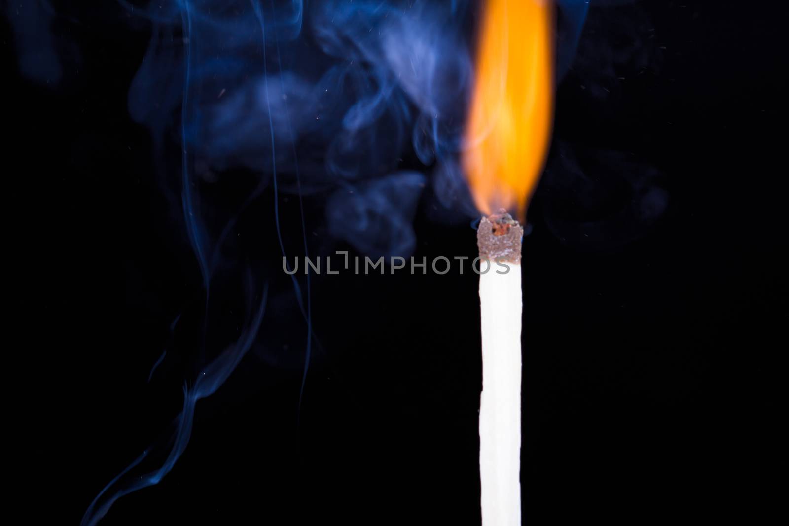 Burning match flame and smoke on dark background.