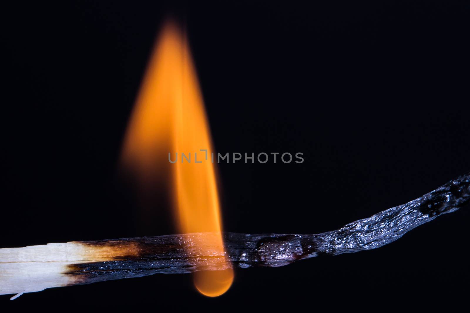 Close up of burning, flaming match on fire against black background.