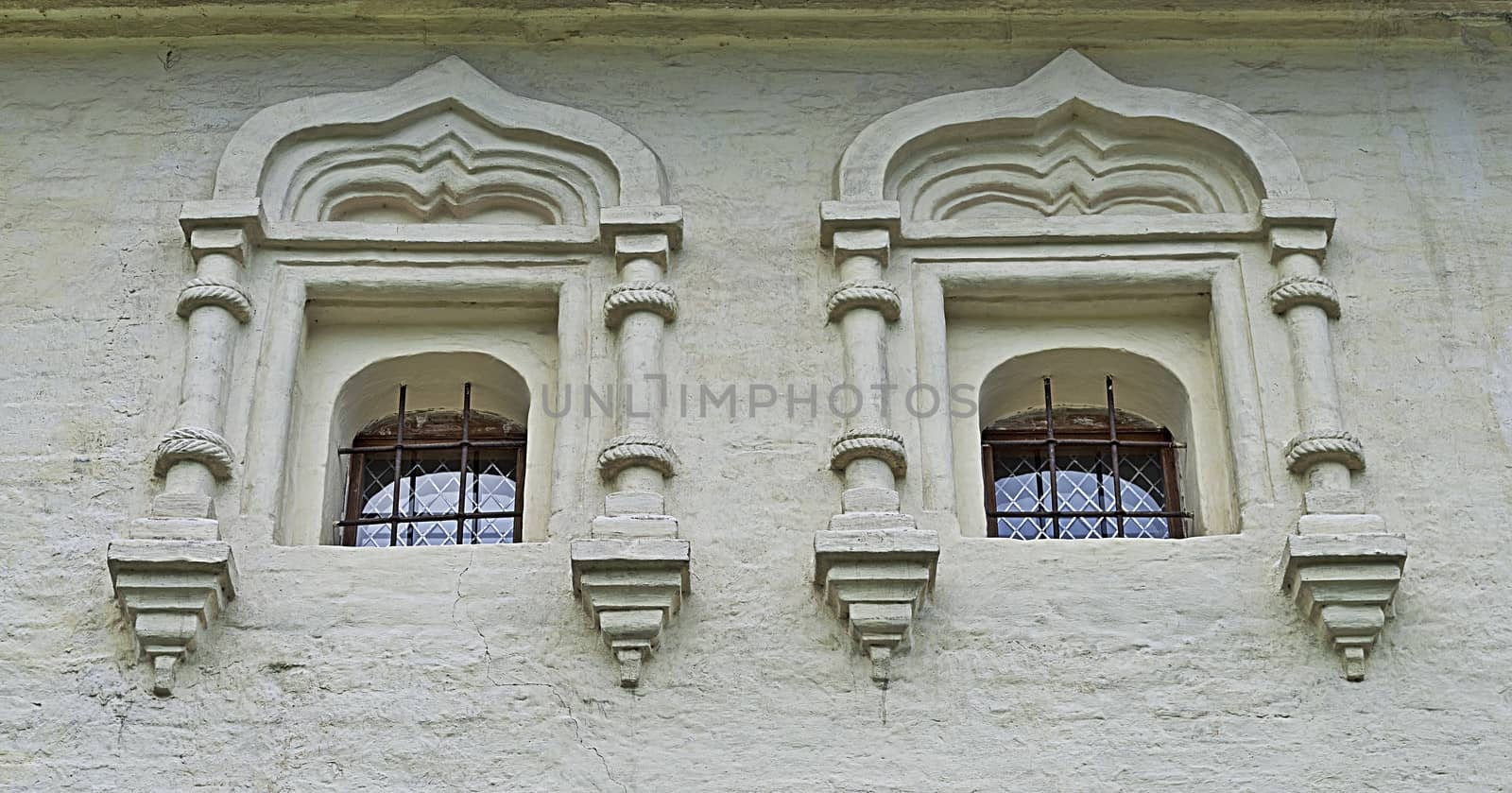 Two small  windows with bars on the white wall in ancient russian monastery