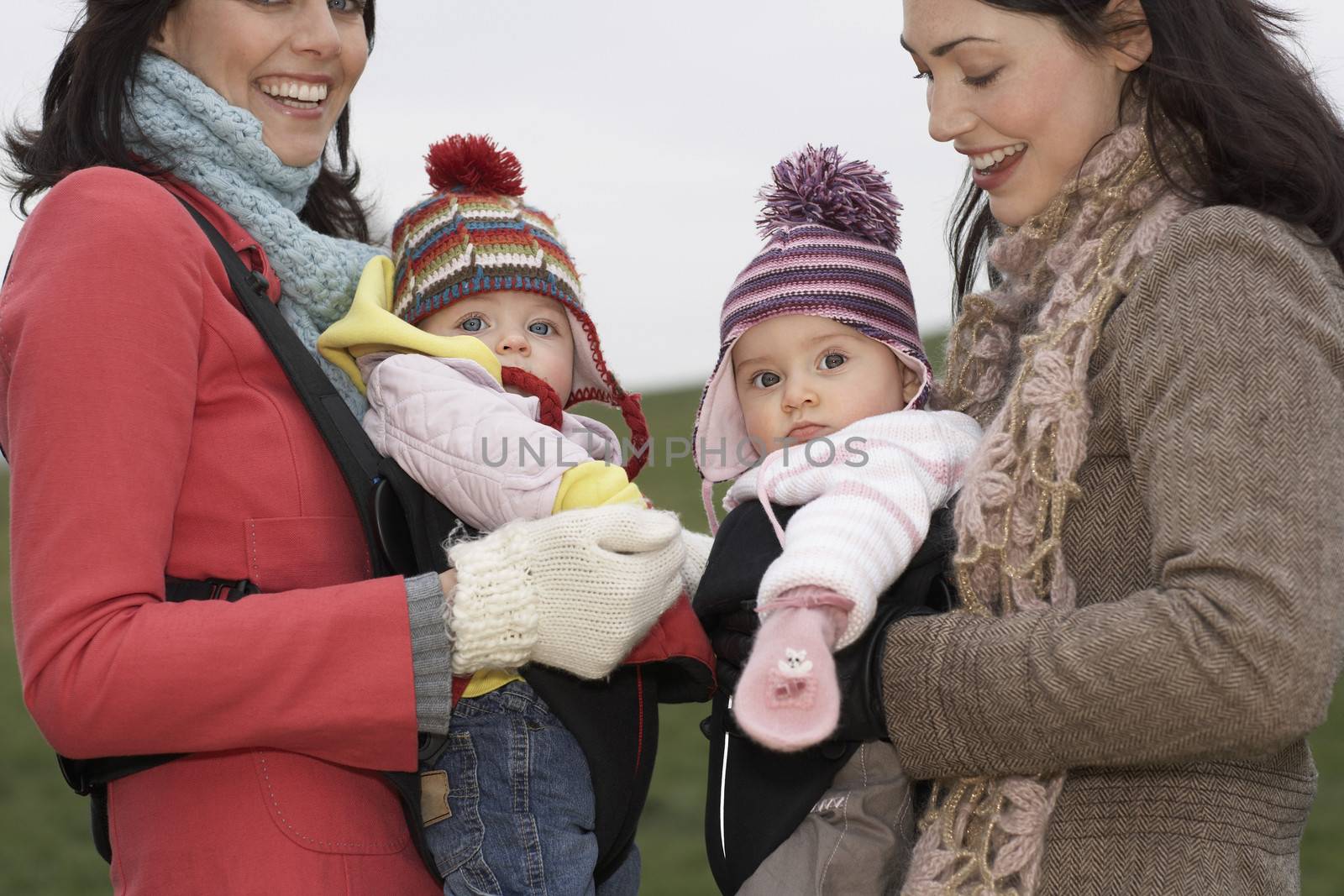 Two mothers in park with babies in slings standing face to face (mid section) by moodboard