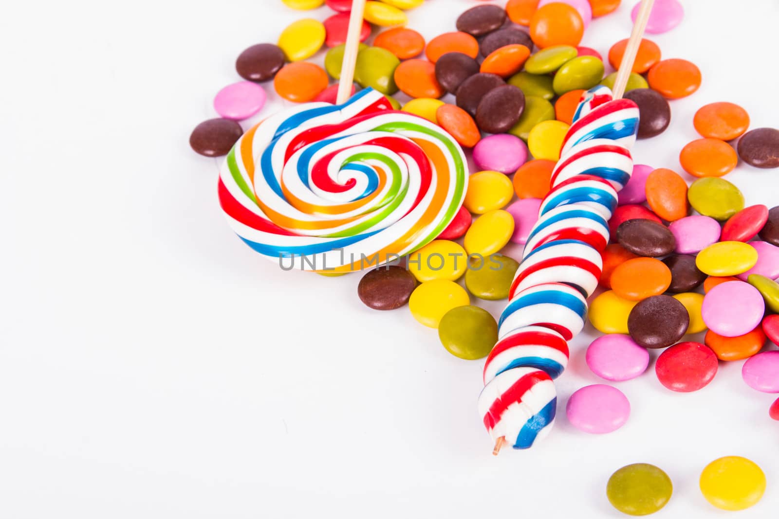 Colorful spiral lollipop candy on stick and little sugars with copy space, isolated on white background.