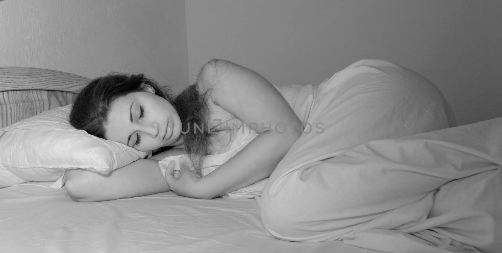beautiful girl with long brown hair sleeping in the white bed in bw color