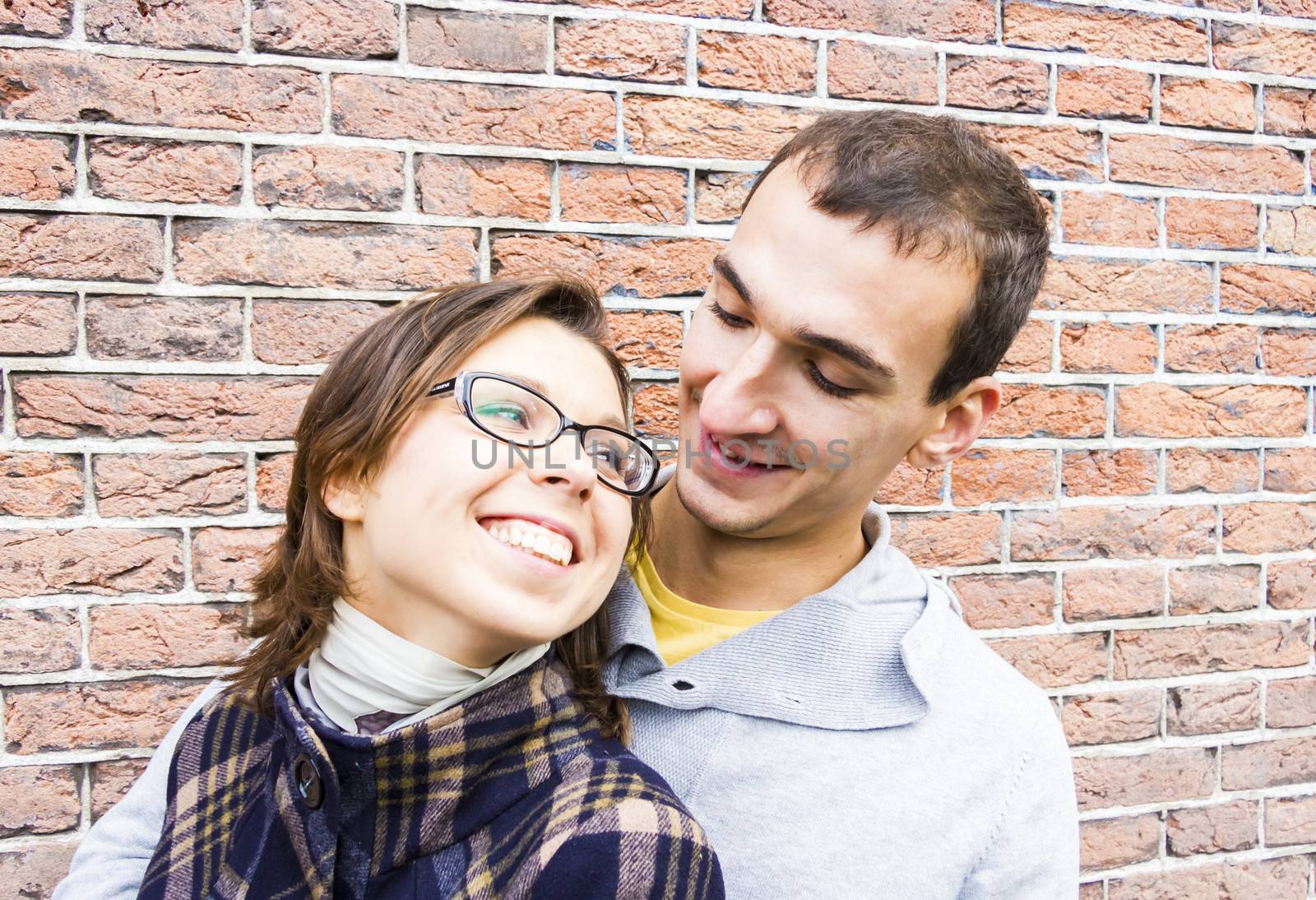 Portrait of love couple embracing looking happy against wall by Tetyana