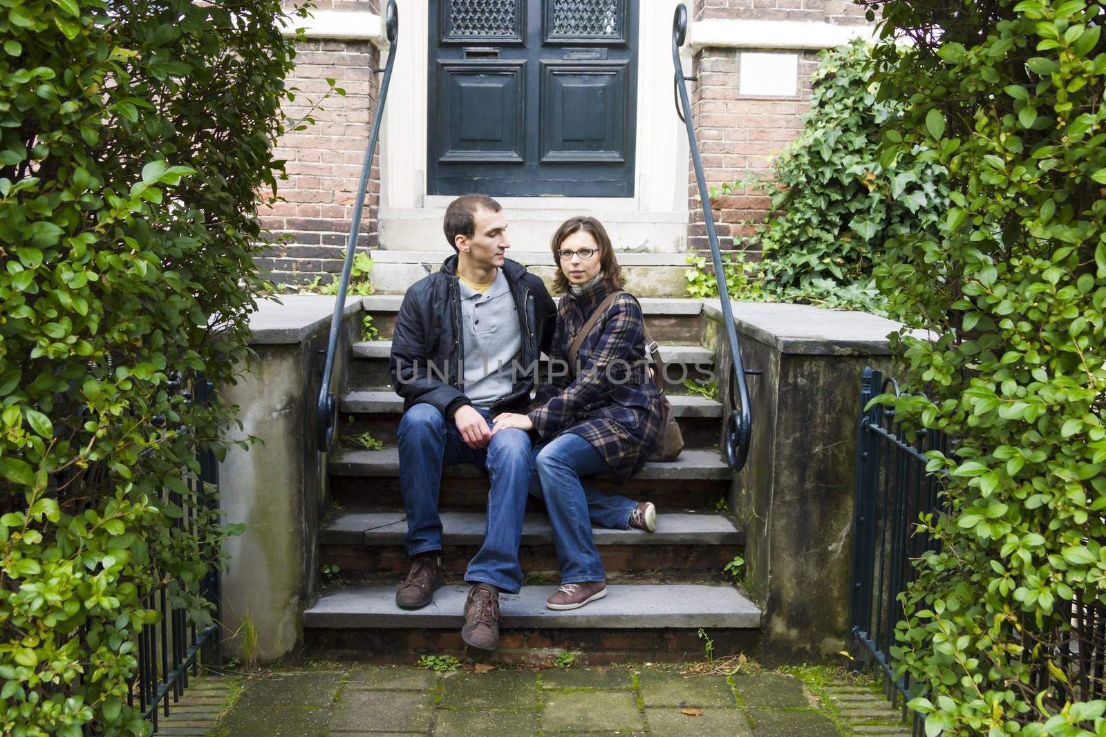 Portrait of love couple sitting on traditional Dutch porch looking happy by Tetyana