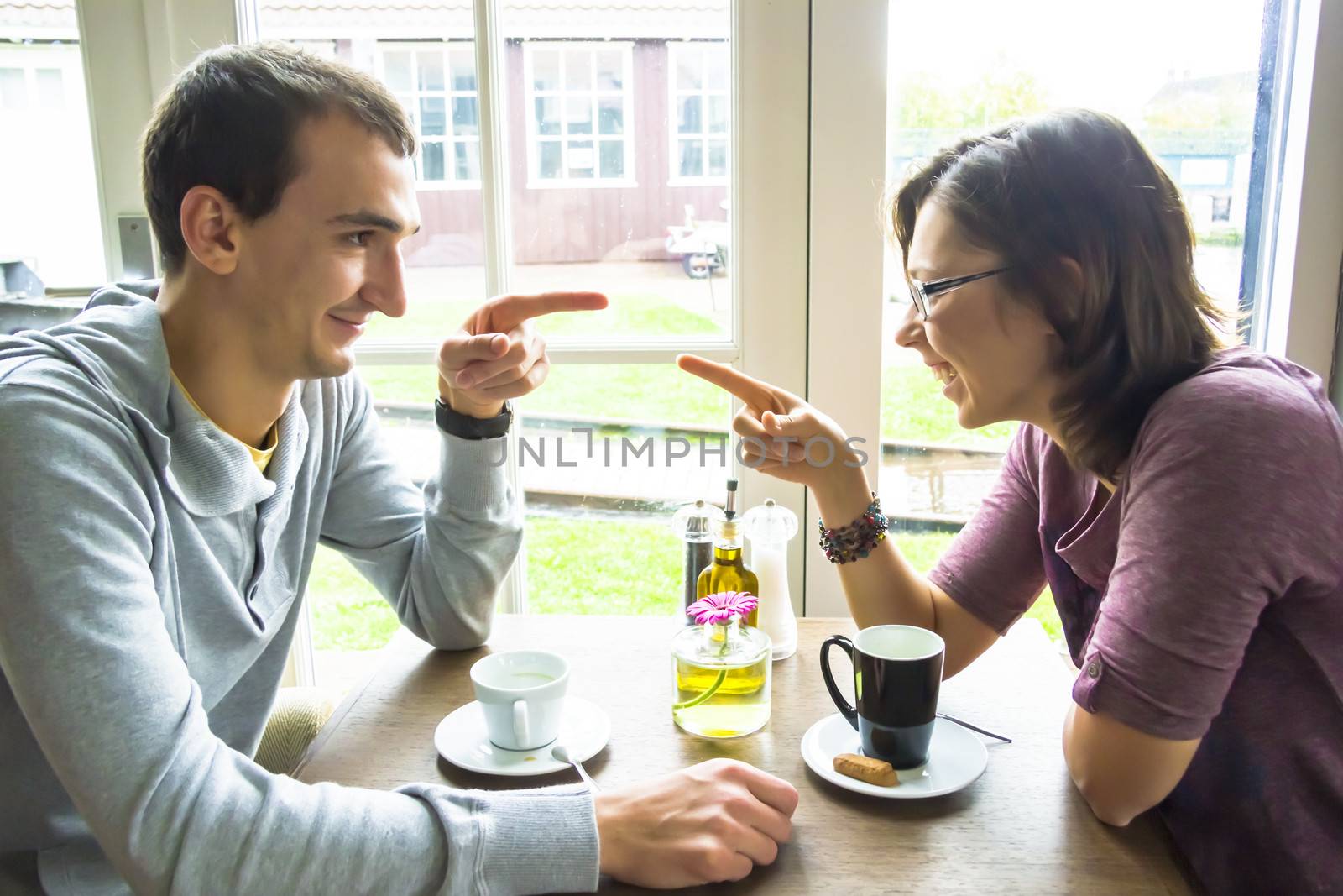 Young man and woman pointing each other while sitting at cafe by Tetyana