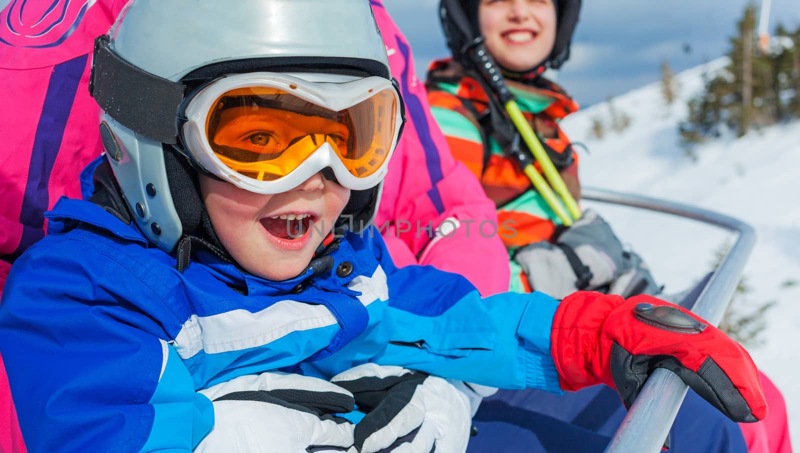 Portrait of happy girl in ski goggles and a helmet with his sister on the ski lift