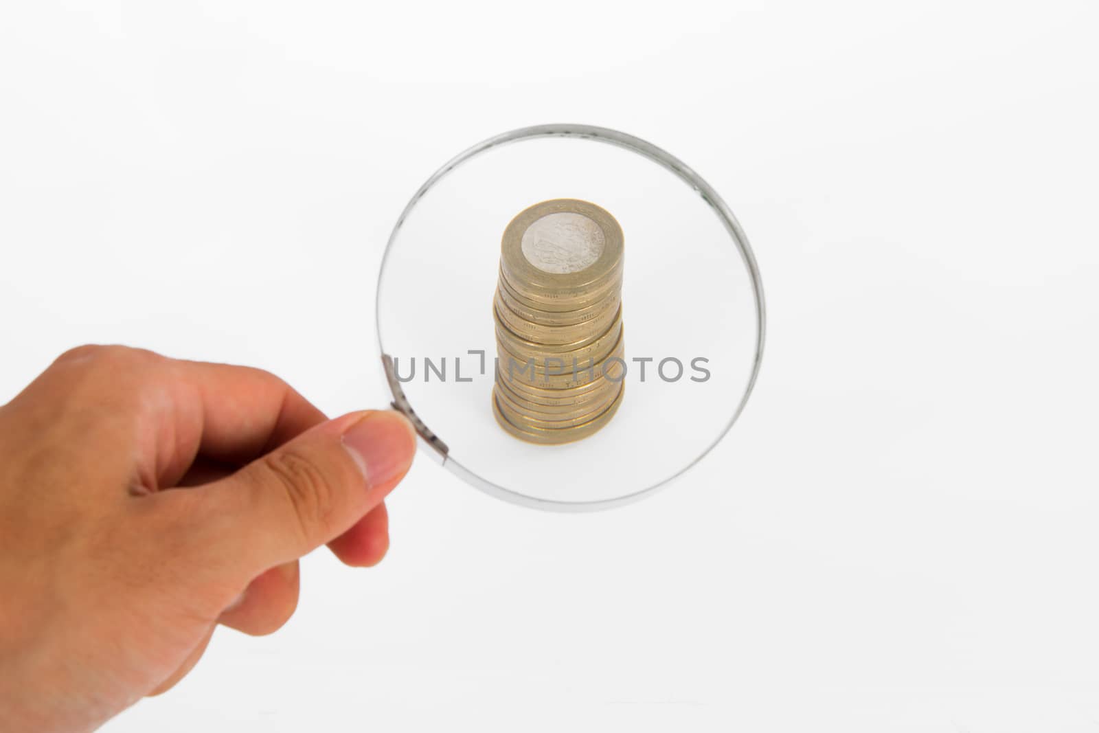 Hand holding magnifying glass and focused on coins, isolated on white background.
