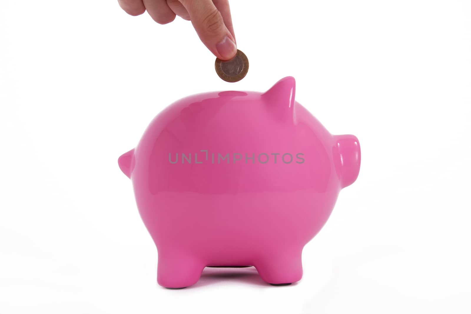 Coin holding by a human hand, fingers and pink piggy bank standing, isolated on white background.