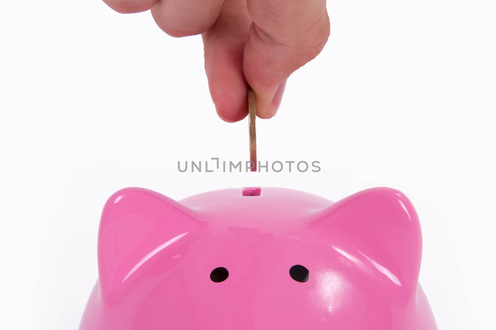 Coin holding by a human hand, fingers and pink piggy bank, isolated on white background.