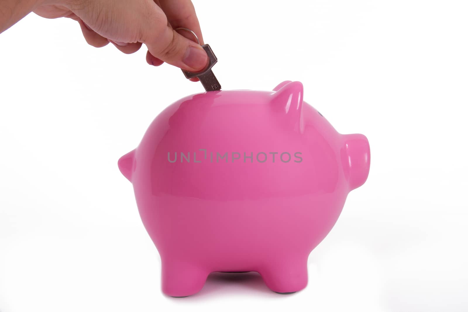Home key holding by a human hand, fingers and pink piggy bank standing, isolated on white background.