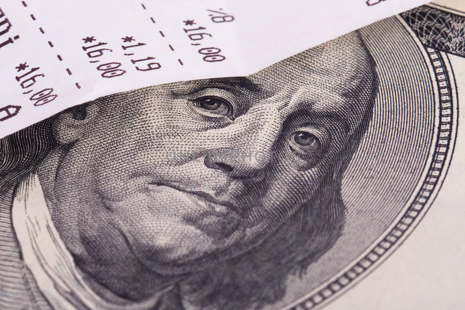 Macro view of cash register receipt and one hundred dollar bill.