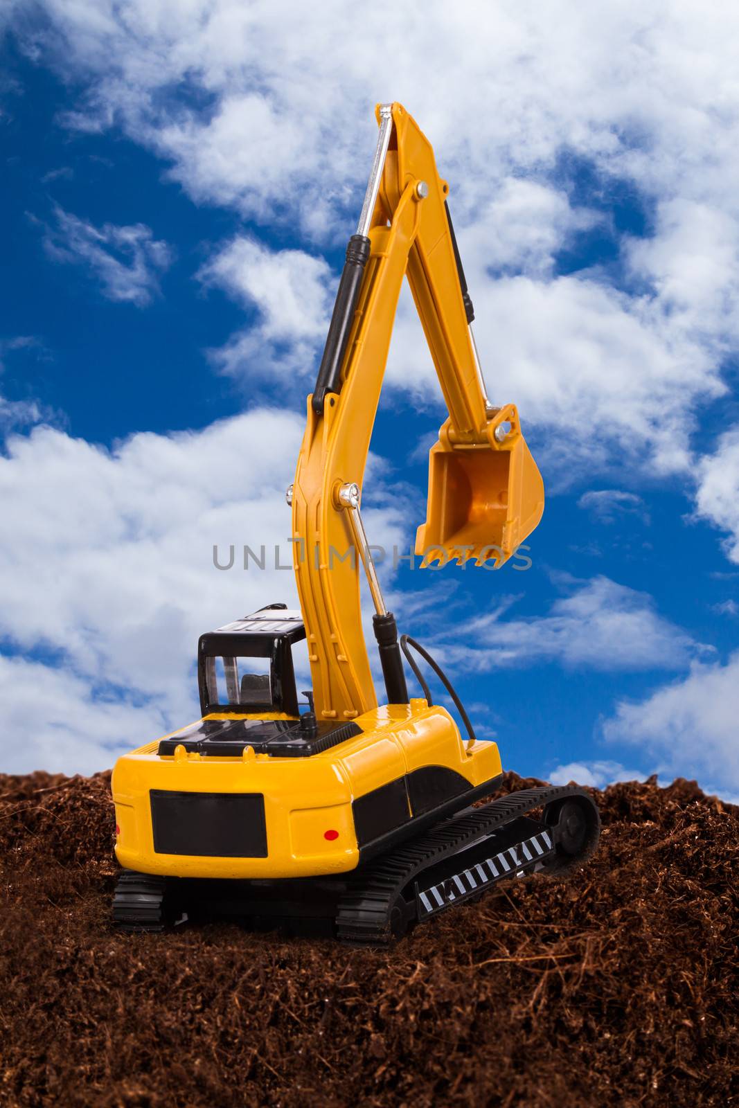 Construction machine, excavator on pile of soil digging a trench, cloudy sky background.