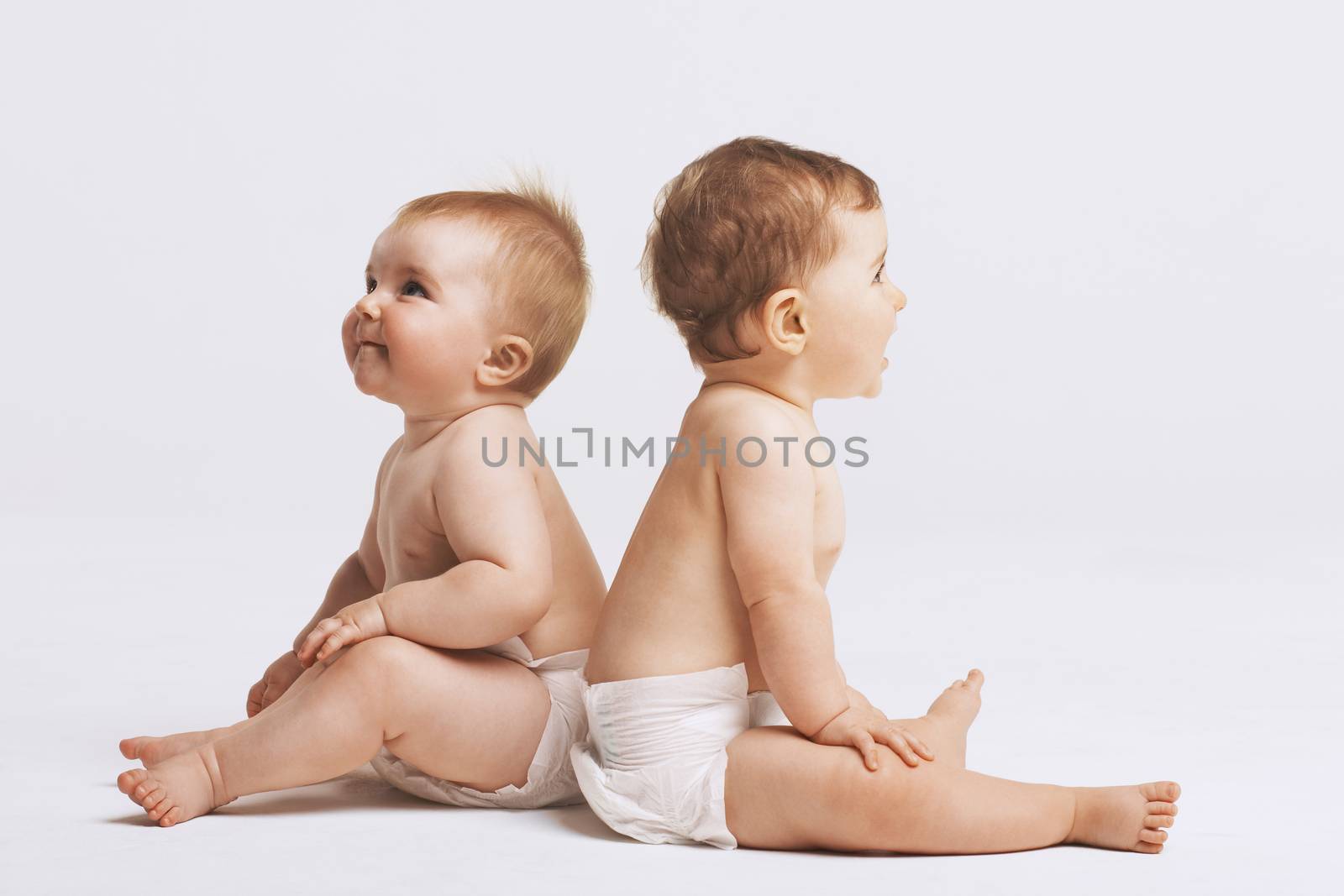 Side view of babies sitting back to back on white background by moodboard