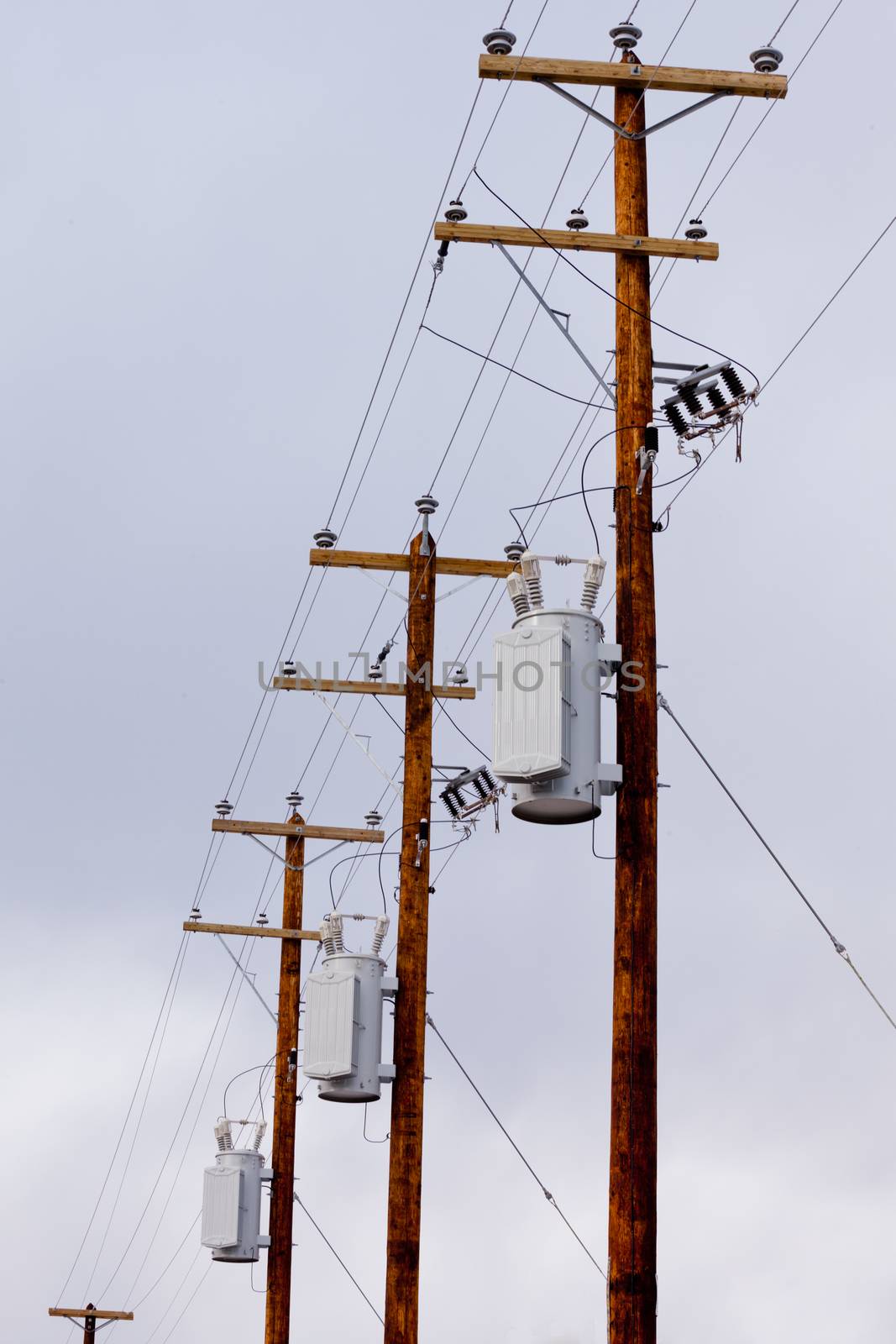 Row utility poles hung with electricity power cables and transformers for residential electric power supply