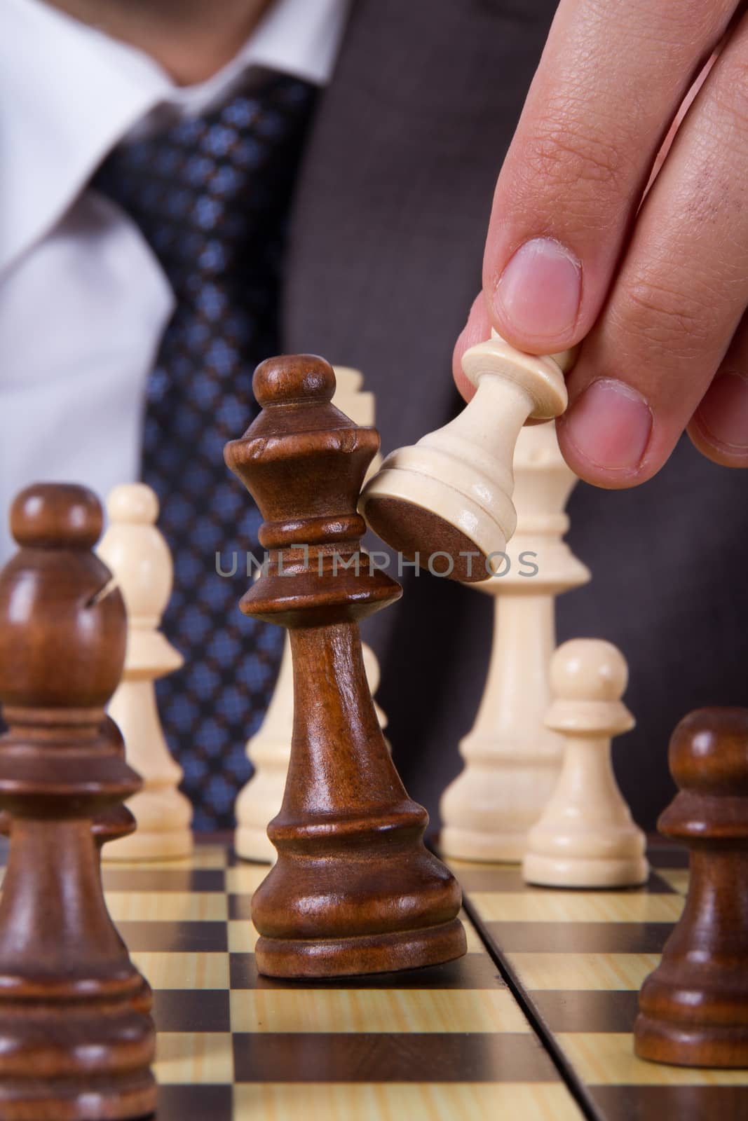 Businessman holding pawn, hitting and defeating opponent king on chess board.