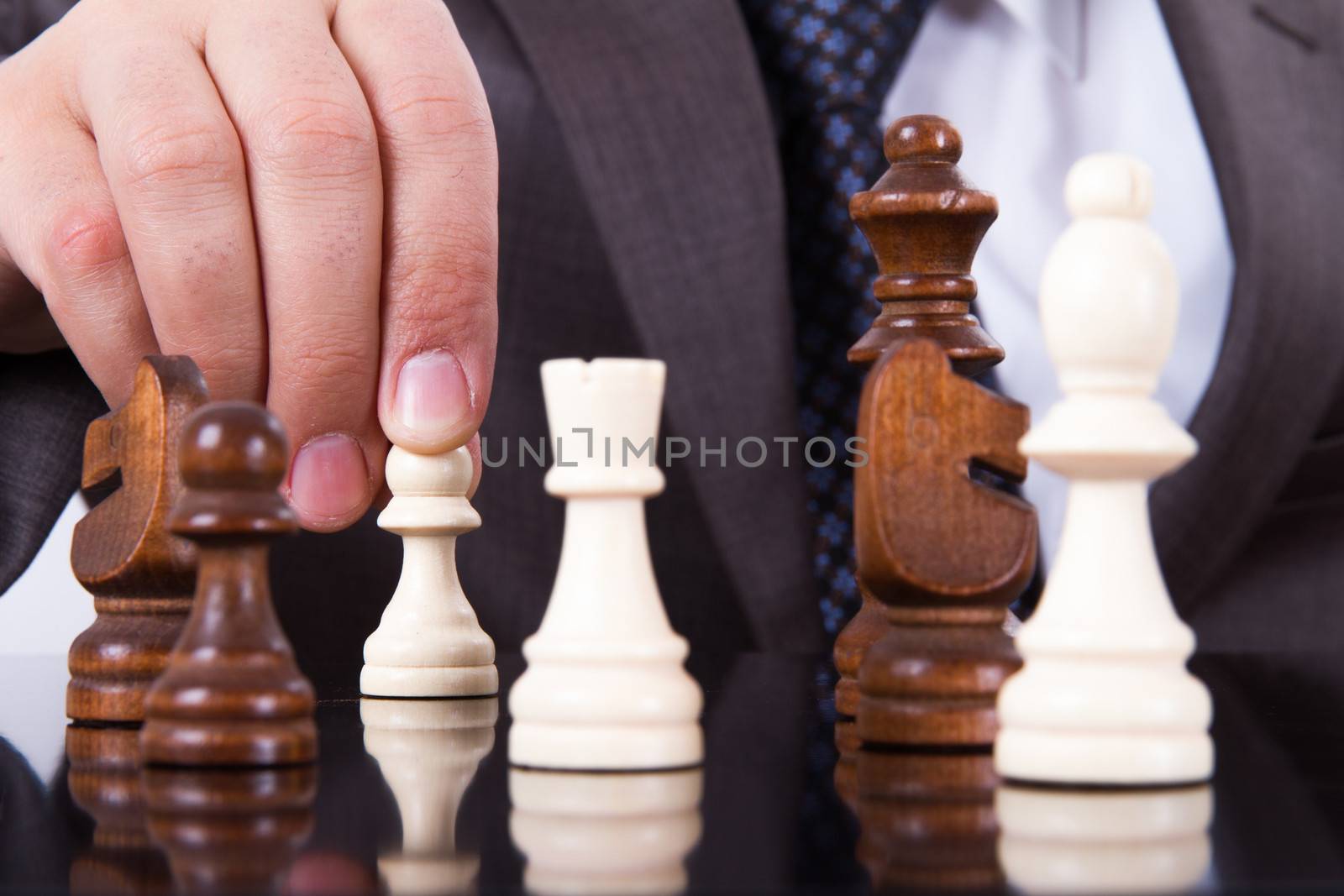 Businessman holding pawn for move on dark reflective table.