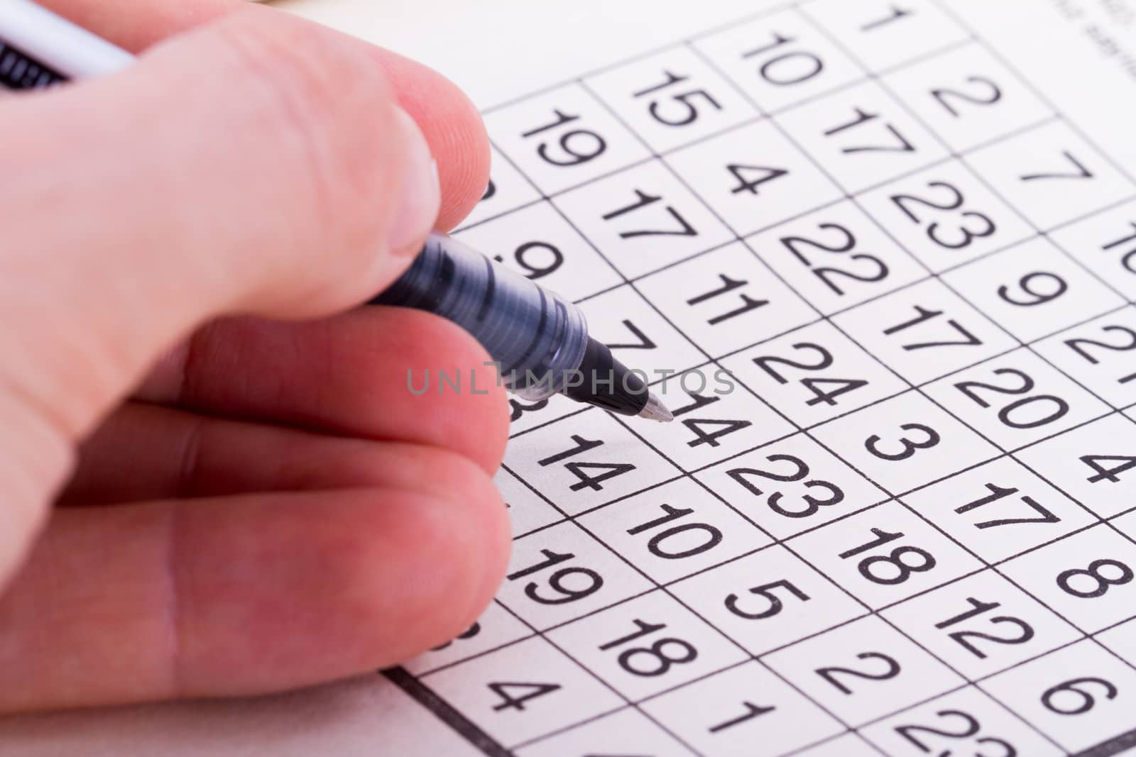 Close up of numbers crossword puzzle with hand holding black pen.