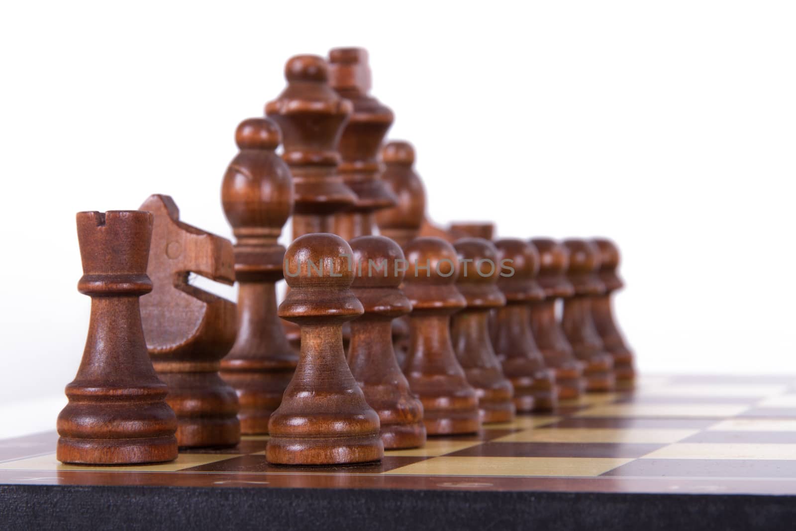 Chess board with starting positions aligned dark wooden chess pieces, isolated on white background.