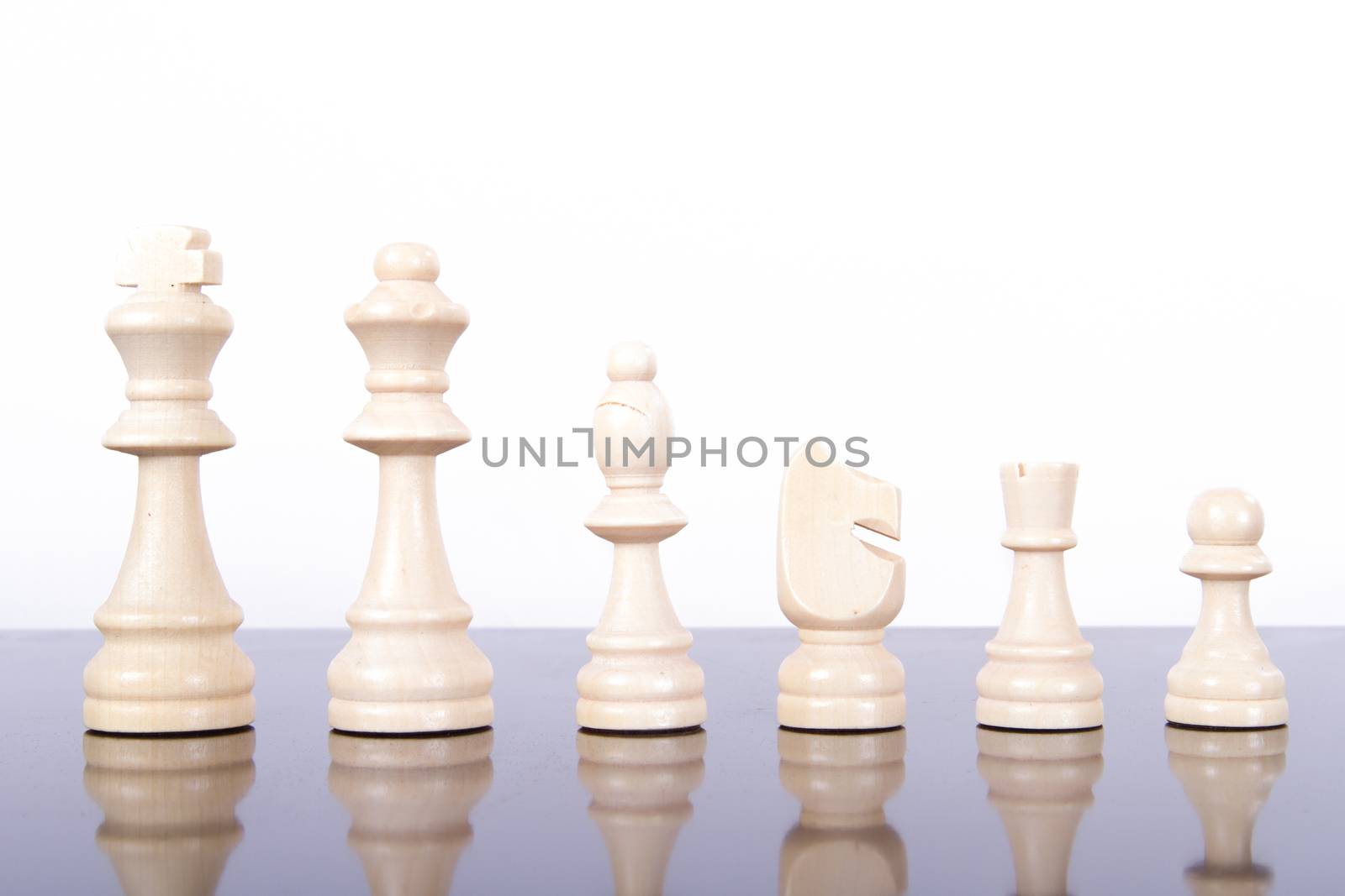 Full set of yellow wooden chess pieces on reflective glass table, isolated on white background.