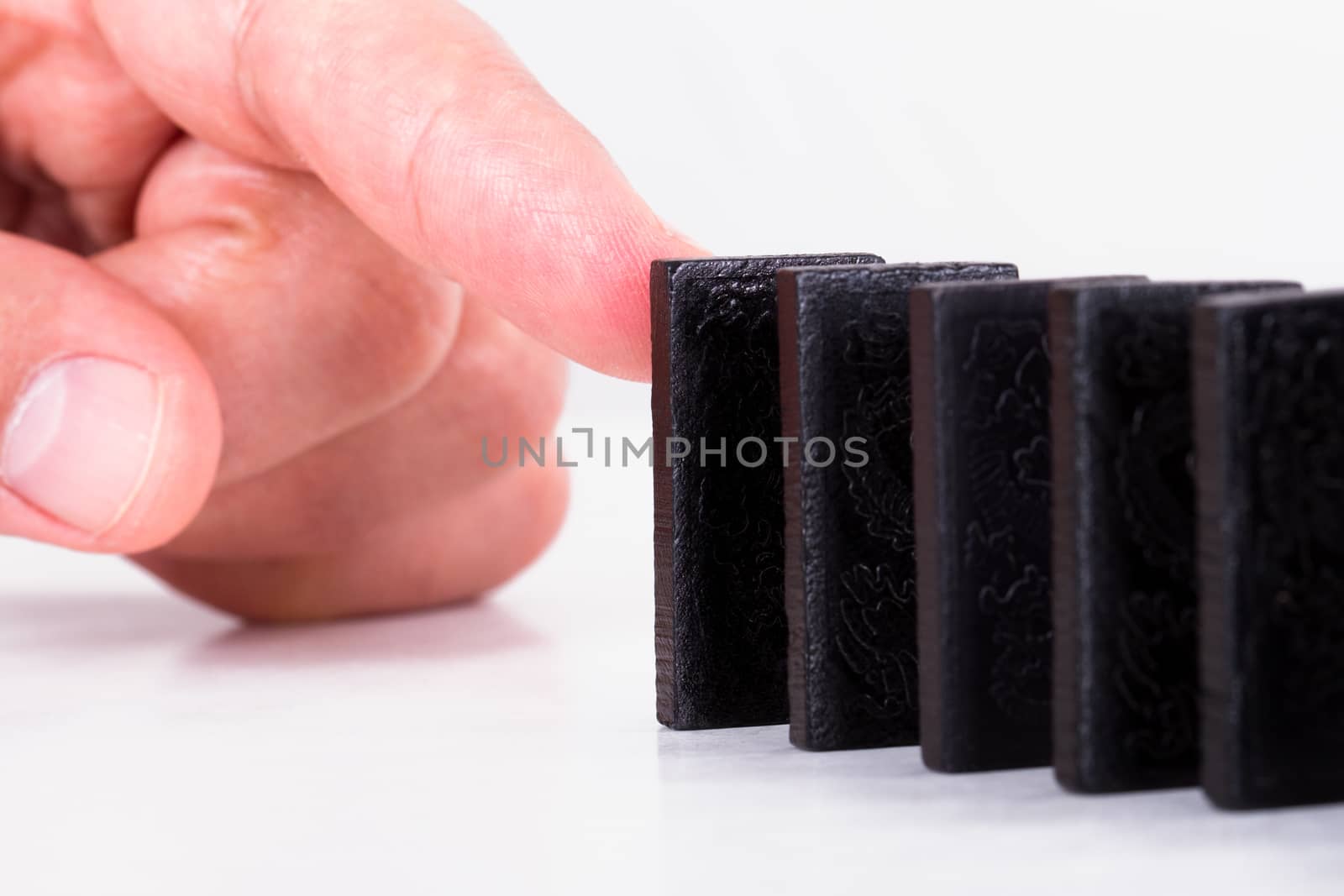 Finger pushing black dominoes, isolated on white background.