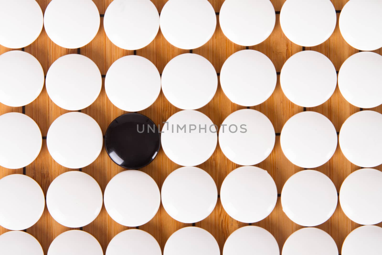 Black stone standing out from white pieces on Chinese go game board.