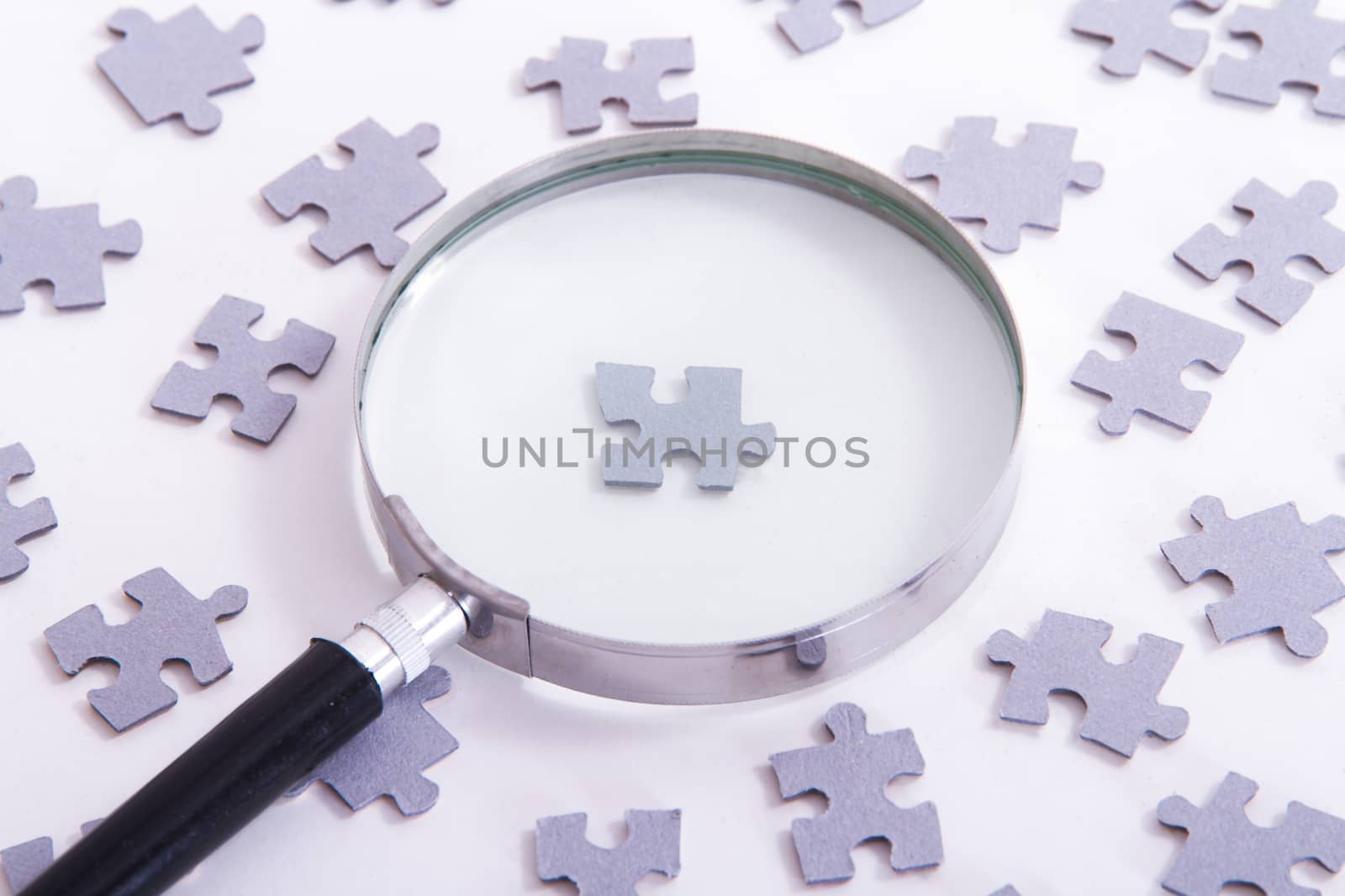 Hand holding classic style magnifying glass and searching leader puzzle piece among others on white.