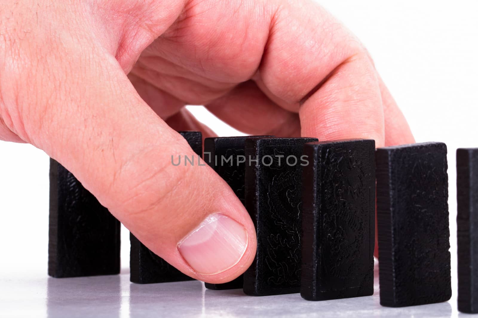 Hand holding black domino and building a line from dominoes, isolated on white background.