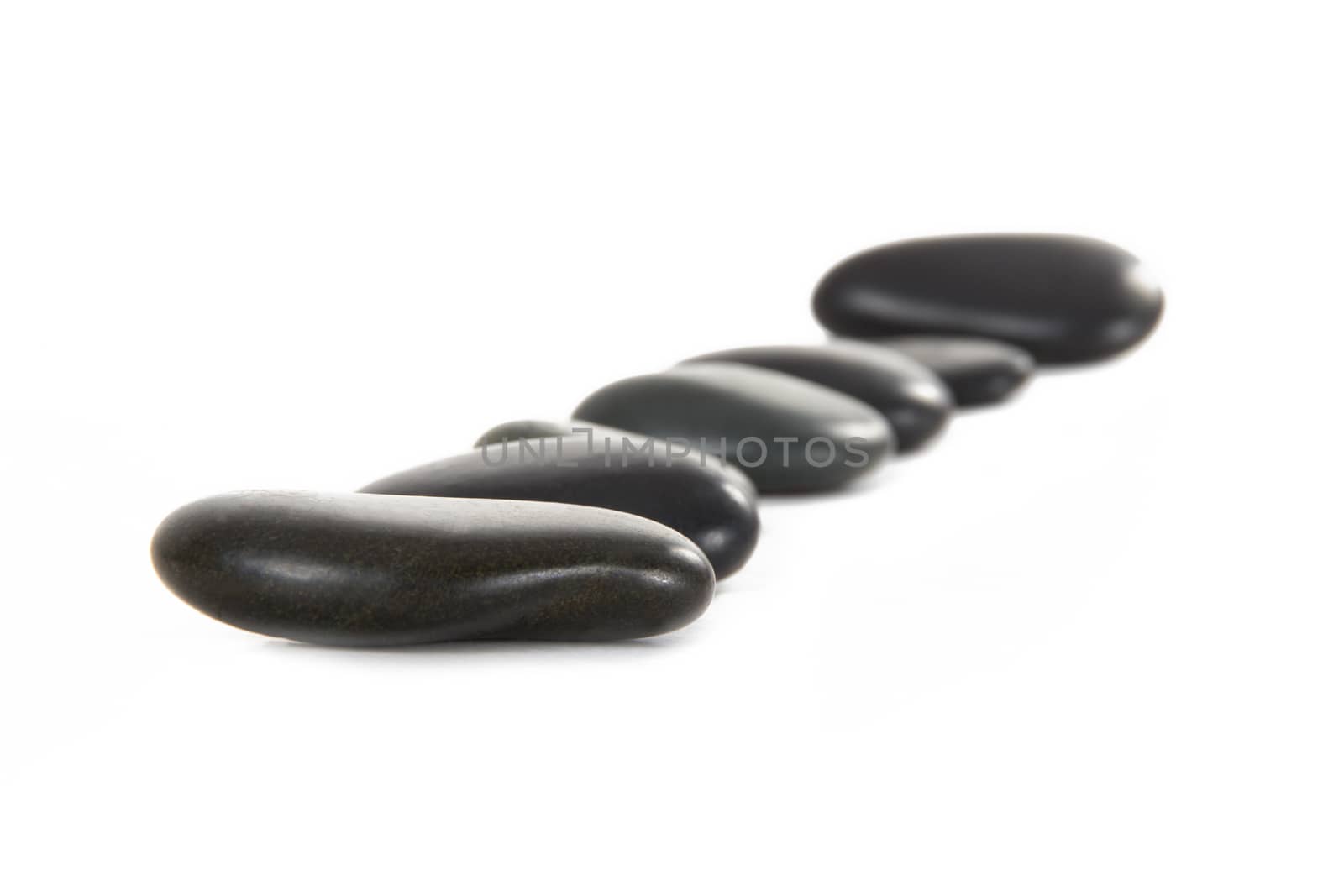 Black massage stones in a row, depth of field, isolated on white background.