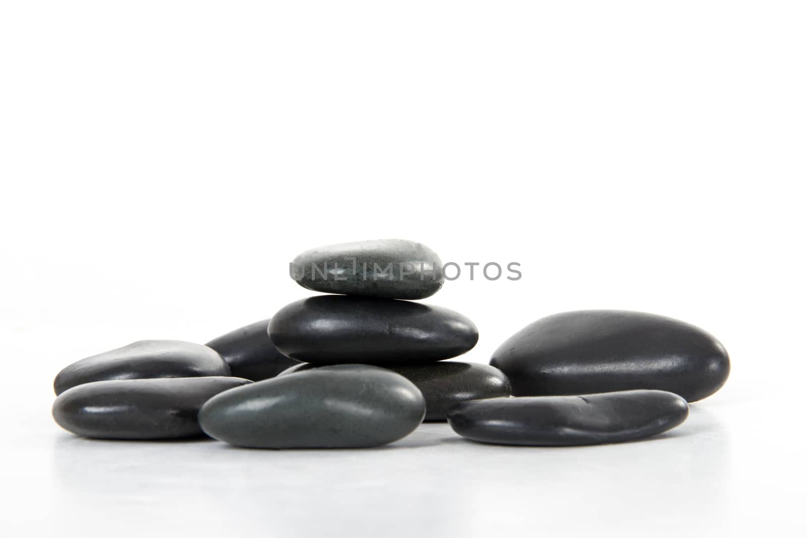 Black massage stones stacked, isolated on white background.