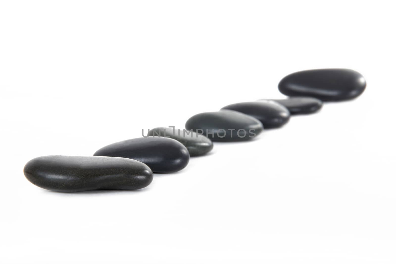 Black massage stones in a row, isolated on white background.