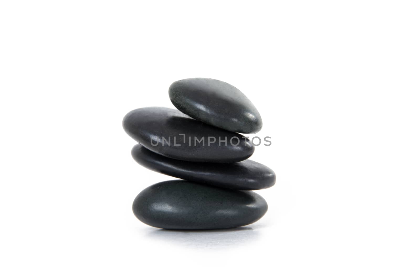 Four black massage stones stacked on balance, isolated on white background.