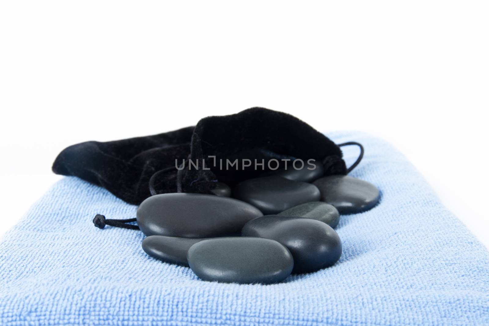Black massage stones with soft case and blue towel, isolated on white background.
