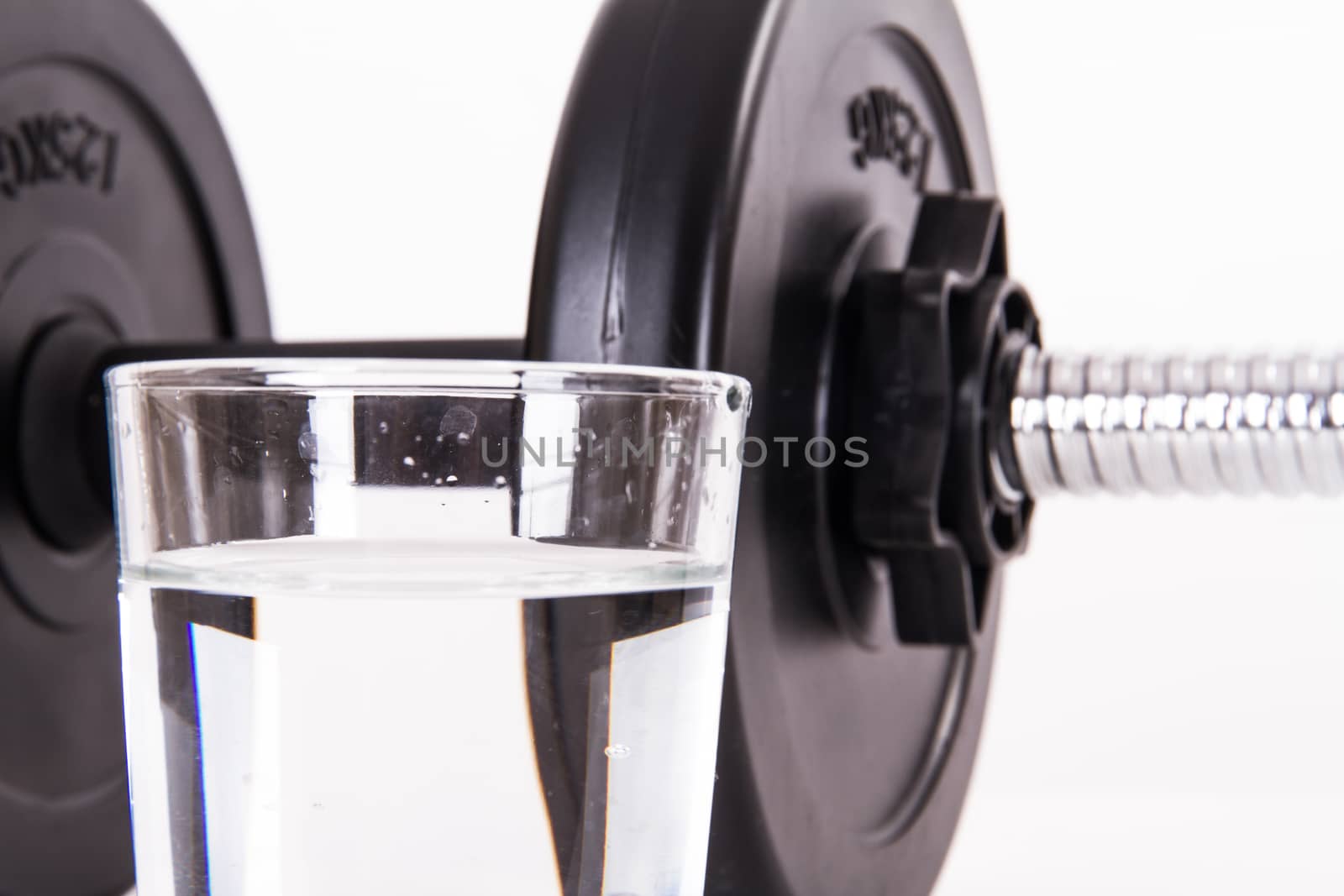 Close up of black gym barbell, dumbbell with disks and glass of water, isolated on white background.