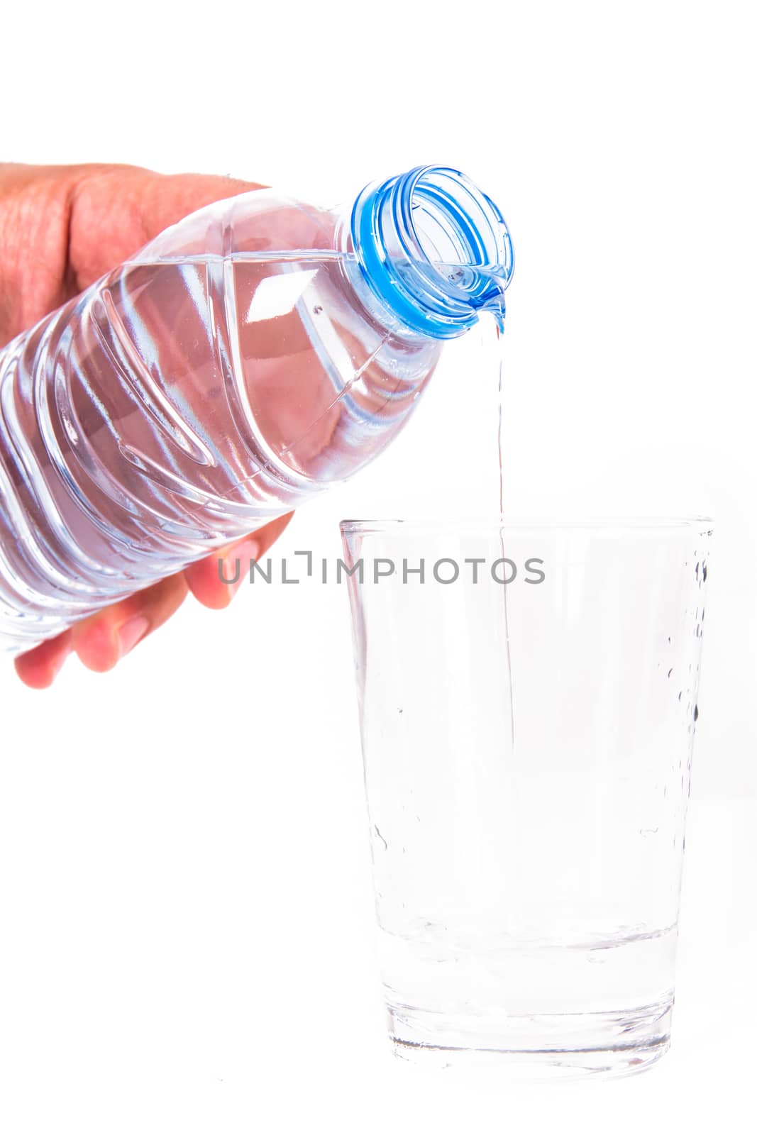 Water pouring into glass from plastic bottle, isolated on white background.